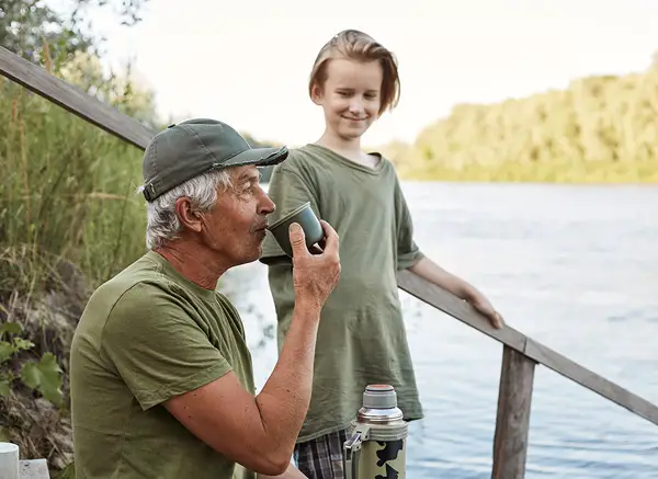 older man and boy sitting on the bank of a river