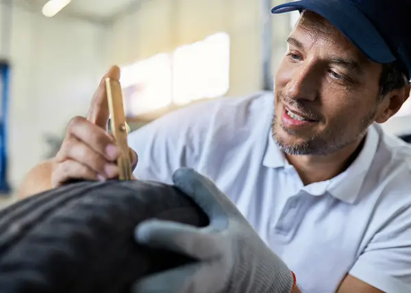 man measuring depth of tire tread in a shop